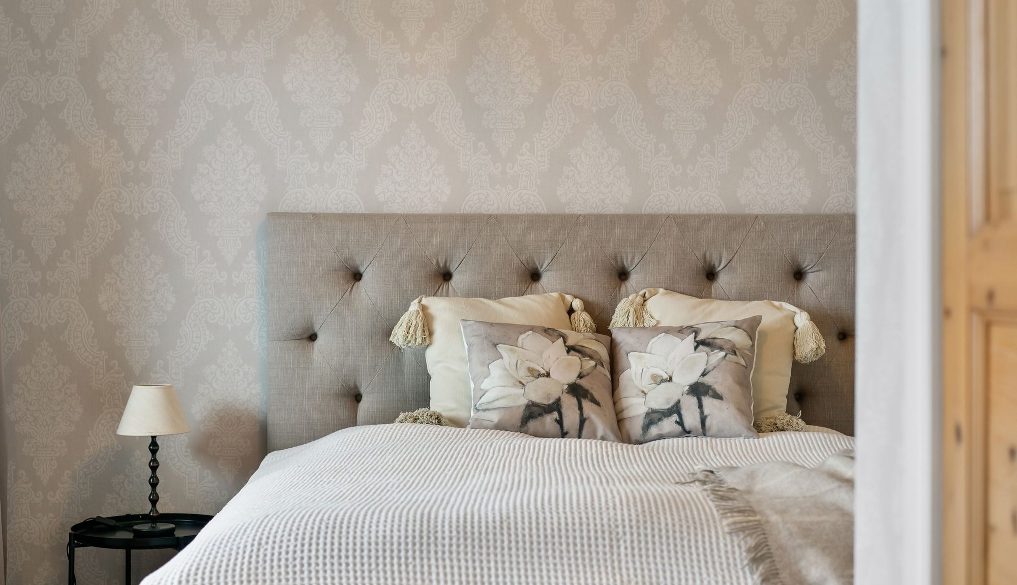Subtle tonal luxury bedroom with softly patterned wallpaper and an upholstered headboard