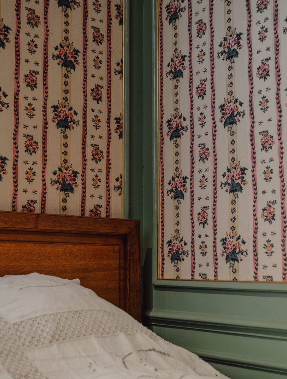 Vintage bedroom with floral and stripe wallpaper beside a green-painted wall