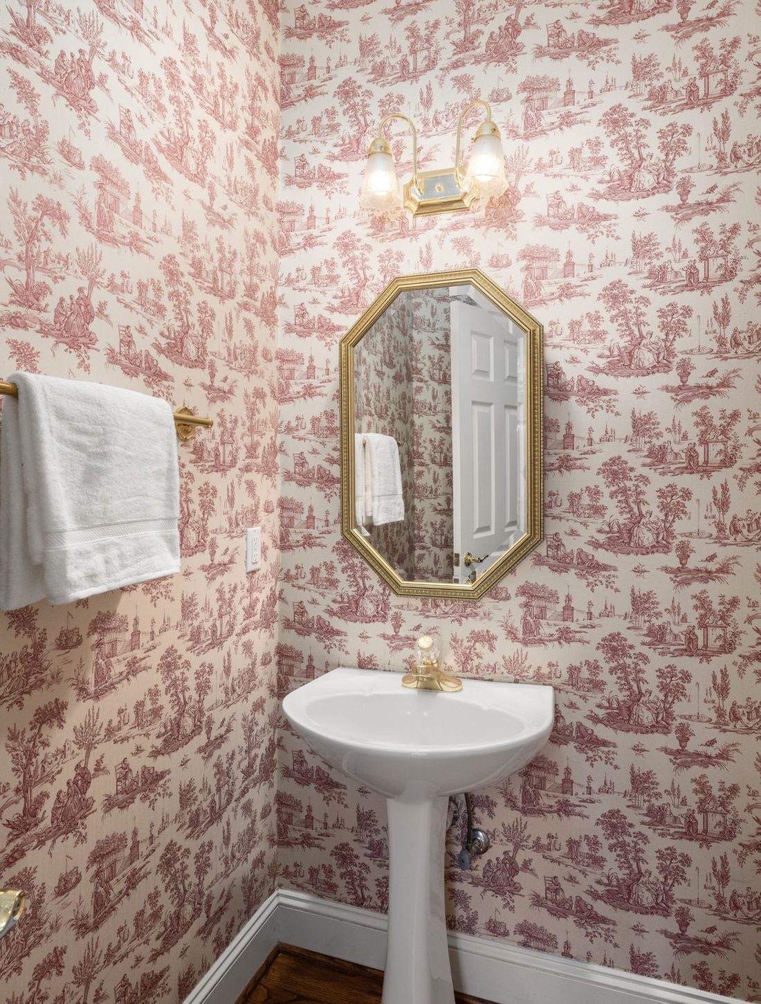 Powder room wrapped in pink toile chinoiserie wallpaper with an octagonal mirror