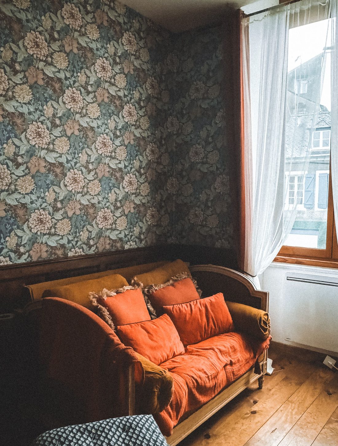 Vintage room with teal small-floral wallpaper and an orange-cushioned bench