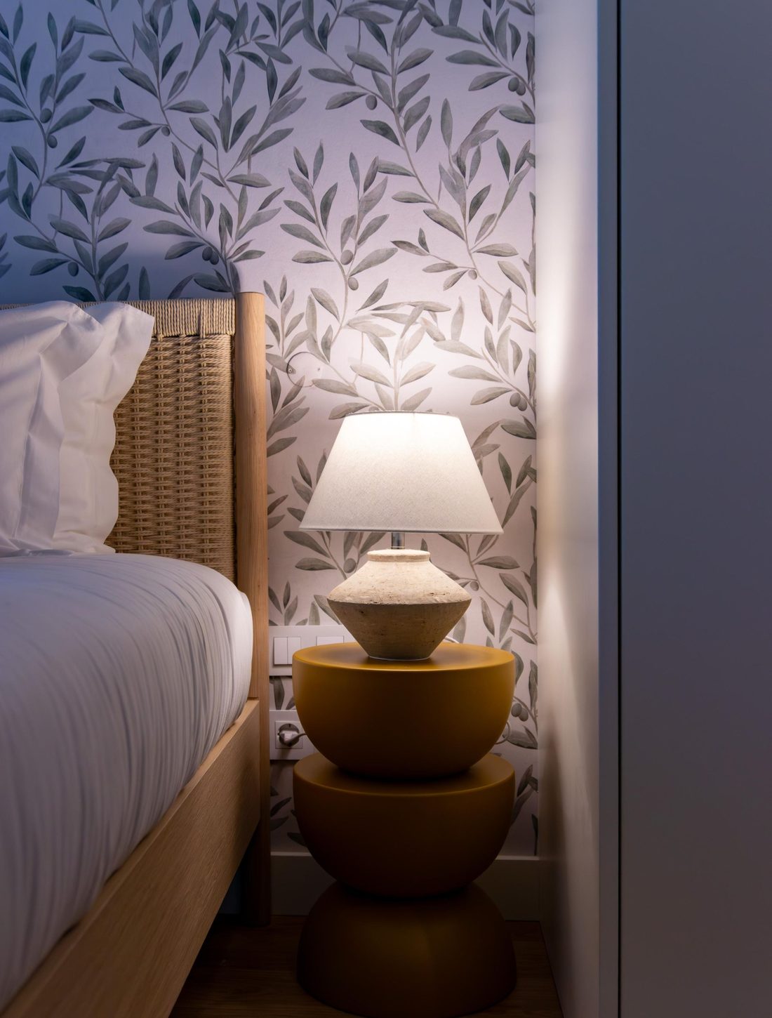 Bedroom with soft lilac-grey leaf botanical wallpaper and a warm lamp