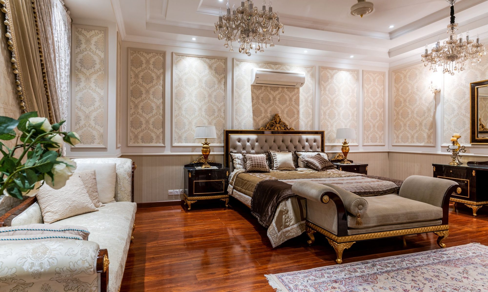Elegant master bedroom with gold damask-panelled wallpaper, chandeliers and polished wood floor