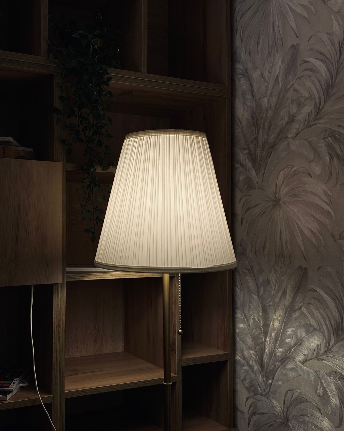 Silvery embossed damask wallpaper glowing behind a pleated floor lamp in a quiet corner