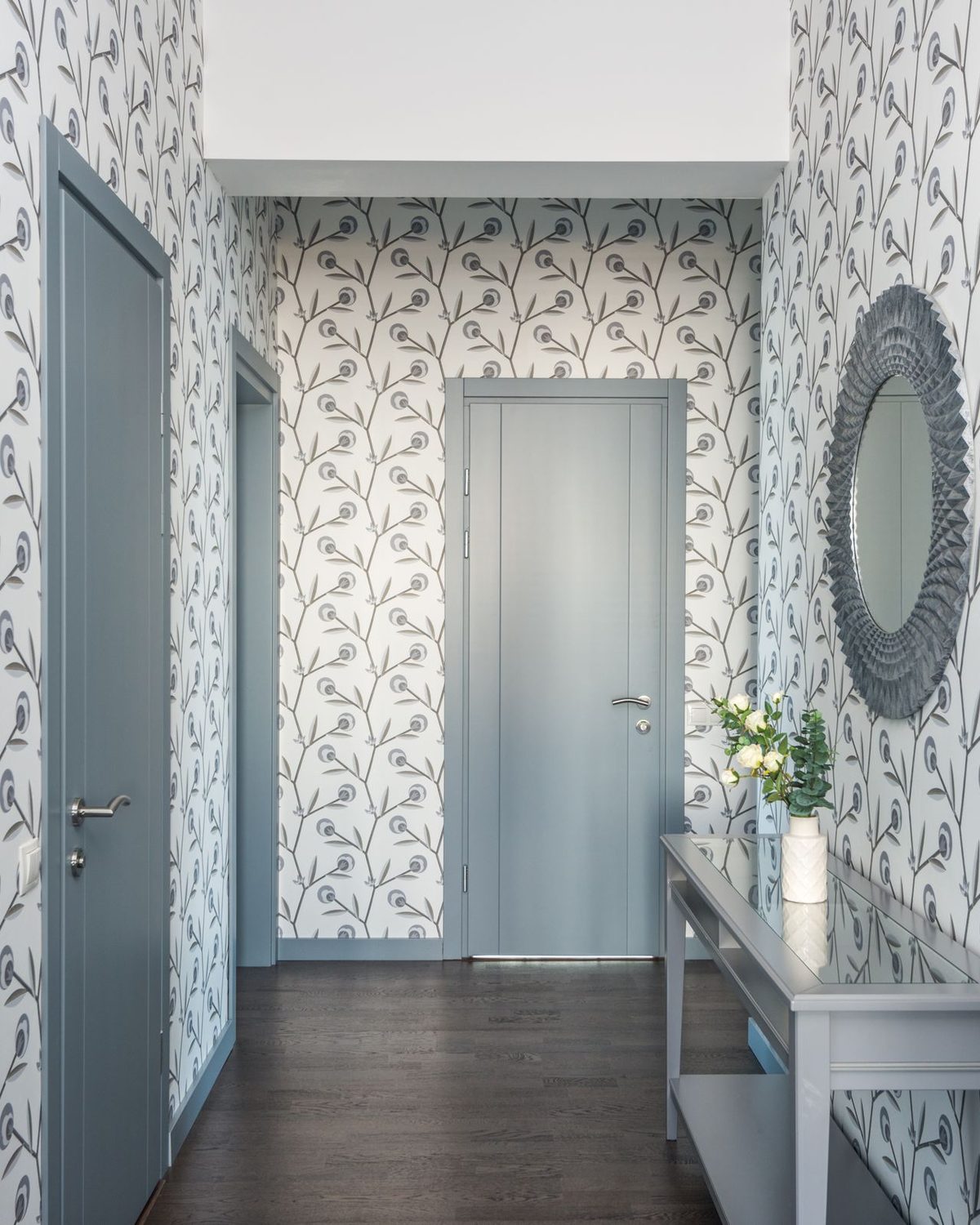 Hallway lined with blue-grey botanical wallpaper, console table and round mirror